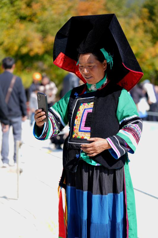 一位彝族妇女手持智能手机 脸上洋溢着自信的笑容