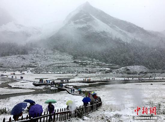 9月20日，受冷空气影响，四川甘孜州稻城亚丁景区雪花飘舞，大雾弥漫，山峰披上白纱，银装素裹。正在景区内游玩的海内外游客纷纷用手机记录雪景，并拍照留念。钟欣 摄